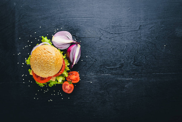 Hamburger with cheese, meat, tomatoes and onions and herbs. On Wooden background. Top view. Free space. - Foto, afbeelding