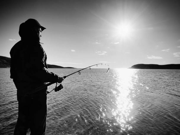 Rybář kontrola rybaření linky a tlačí návnada na tyči. Rybář silueta při západu slunce  - Fotografie, Obrázek