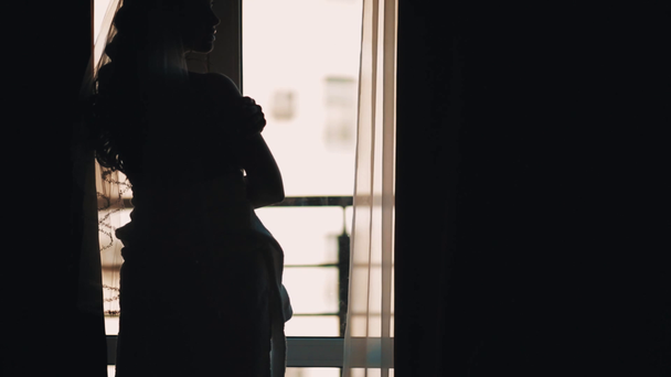 Silhouette of bride woman waiting for groom in front of window - Video