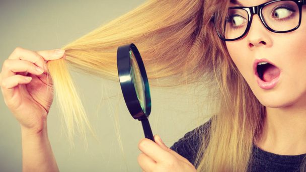 Woman holding magnifying glass looking at hair - 写真・画像