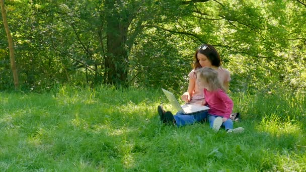 Família Passar tempo juntos ao ar livre usando laptop branco. Duas meninas estão jogando videogames sentados na grama verde no parque da cidade
. - Filmagem, Vídeo