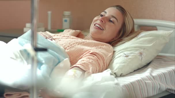 Young female patient lying in hospital bed on drip talking to a doctor - Záběry, video