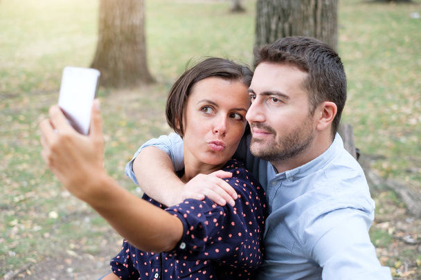 Pareja feliz tomando fotos de selfie sentada en un banco en un parque
 - Foto, imagen