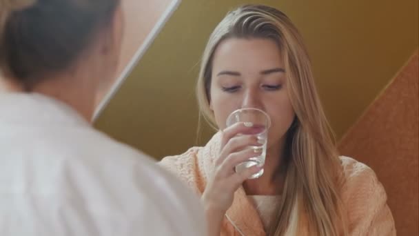 Smiling woman is taking medicine and a glass of water in hospital - Materiał filmowy, wideo