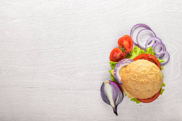 Hamburger se sýrem, masem, rajčaty a cibulí a byliny. Na dřevěné pozadí. Pohled shora. Volné místo. - Fotografie, Obrázek