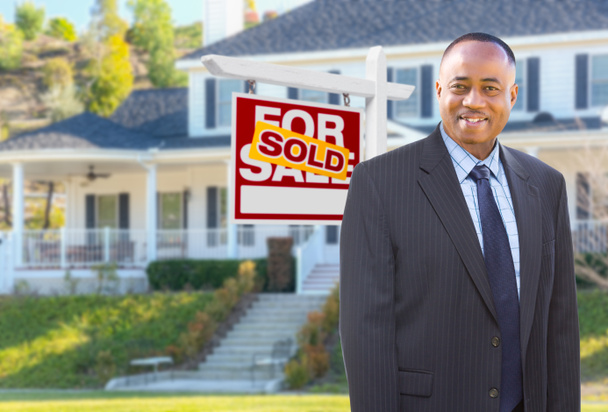 Αφρικανικός Αμερικανός πράκτορας μπροστά από το όμορφο έθιμο σπίτι και πωλούνται για το σημάδι πώλησης ακινήτων. - Φωτογραφία, εικόνα