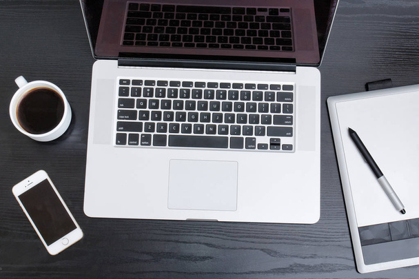 Avoin kannettava tietokone, graafinen tabletti, älypuhelin ja kahvimuki mustalla pöydällä, ylhäältä
 - Valokuva, kuva