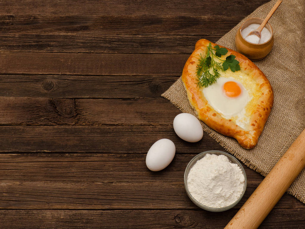 Chaczapuri z jaj na worze, soli, mąki, jajka i pietruszki na drewnianym stole, miejsca na tekst - Zdjęcie, obraz