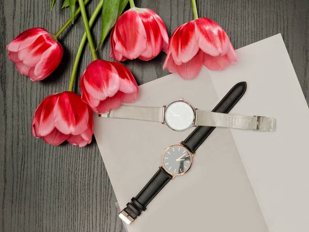 Dois relógios de pulso numa folha cinzenta e tulipas. Conceito na moda, vista superior
 - Foto, Imagem