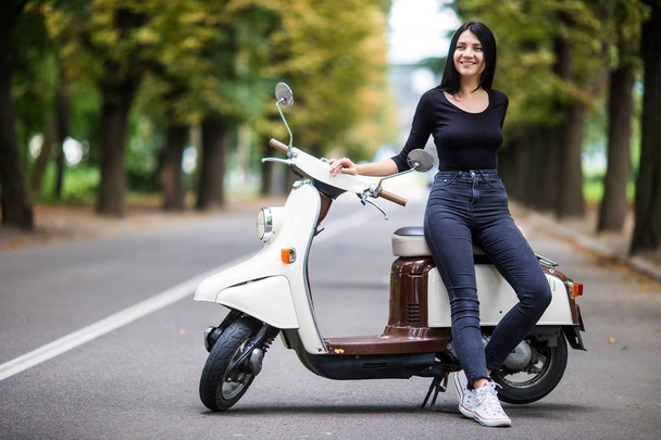 Příležitostné mladá žena sedící na moto skútrů na úzké uličce ve městě. - Fotografie, Obrázek