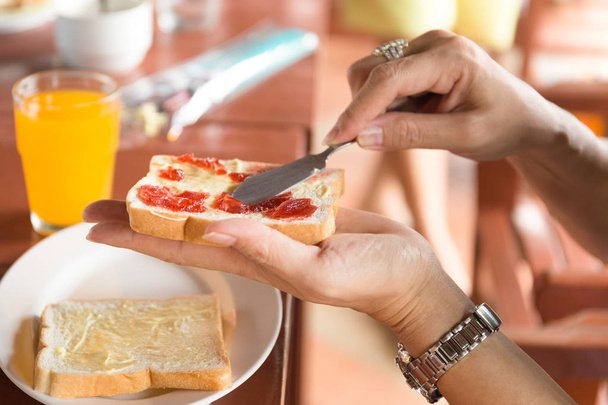 Breakfast with woman hand spreading strawberry jam on top slice  - Photo, image