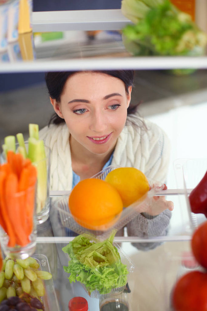 Portrait of female standing near open fridge full of healthy food, vegetables and fruits. Portrait of female - Foto, Imagem