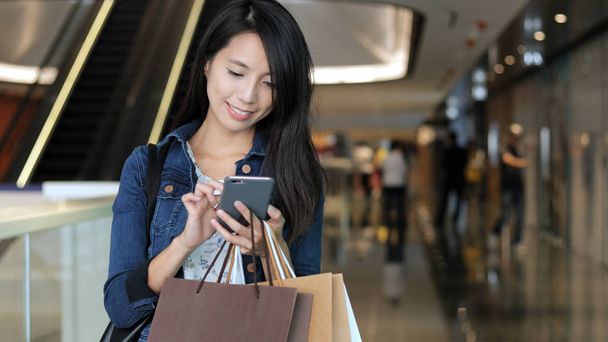 Mulher usando celular e segurando sacos de compras
 - Foto, Imagem