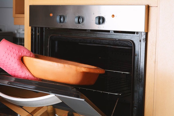 Виймання запеченого лотка з духовки з кухонними рукавичками
 - Фото, зображення