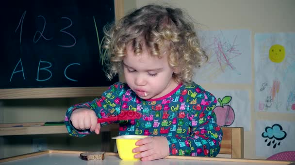 Mädchen essen Lieblings-Joghurt mit Löffel. Kind leckt Plastiklöffel mit Zunge - Filmmaterial, Video