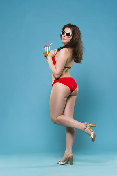 Beautiful young woman in red bikini with cocktail on blue background - Fotoğraf, Görsel