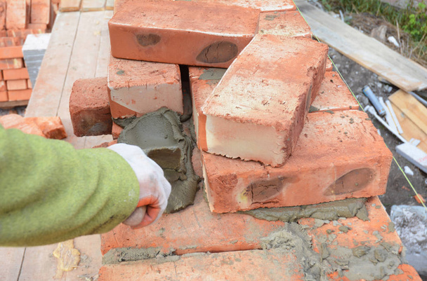 Maurer Arbeiter, der rote Blöcke einbaut und Ziegelmauerwerk abdichtet, fugt Außenwand mit Spachtelkelle ein. Mauerwerk.  - Foto, Bild
