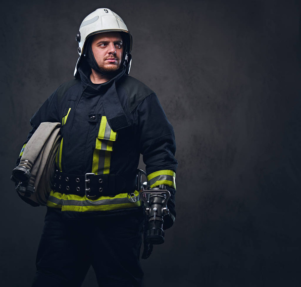 Пожарный в форме держит пожарный шланг
. - Фото, изображение