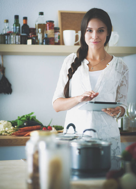 Mutfakta yemek yapmak için tablet bilgisayar kullanan genç bir kadın. - Fotoğraf, Görsel