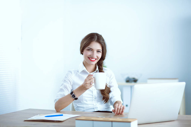 Young businesswoman sitting on the desk with with cup - 写真・画像