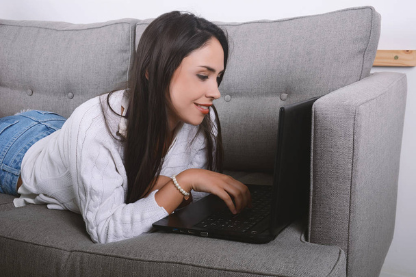 Woman using laptop on couch. - Foto, afbeelding