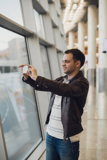 viaggiatore con cellulare all'aeroporto che fotografa il suo aereo. Strutture di controllo del traffico aereo sullo sfondo
 - Foto, immagini