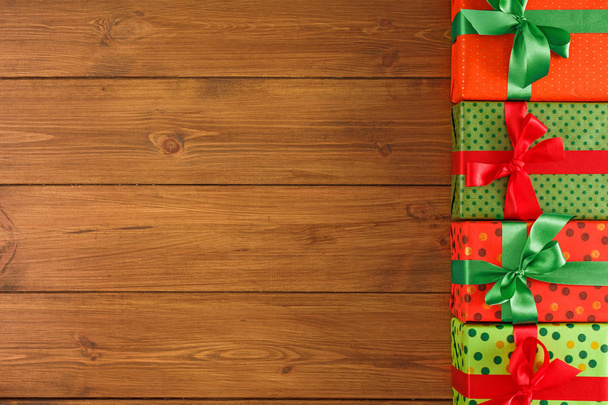 Рождественские подарочные коробки, вид сверху с копировальным местом на фоне деревянного стола. Граница цветных пакетов с красными, зелеными лентами на Рождество
 - Фото, изображение