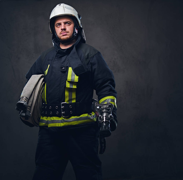 Пожарный в форме держит пожарный шланг
. - Фото, изображение
