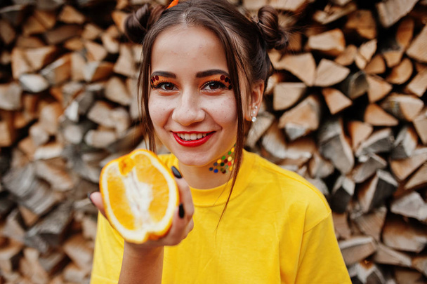 Young funny girl with bright make-up, wear on yellow shirt hold  - 写真・画像