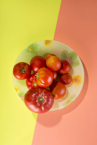 Αφηρημένη νεκρή φύση με τις ντομάτες σε ένα πιάτο σε φόντο κίτρινο-ροζ - Φωτογραφία, εικόνα