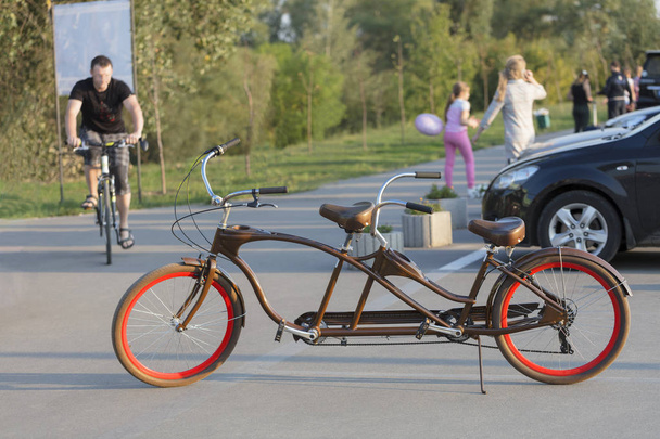 Tandem-polkupyörä, jossa on tulipunainen vanteet, on pysäköity parkkipaikalle illalla aurinko
. - Valokuva, kuva