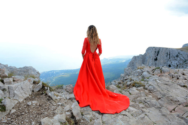 Woman in long red dress on the edge of a cliff in the mountains. Peak of Ai-Petri mountain - Foto, Bild