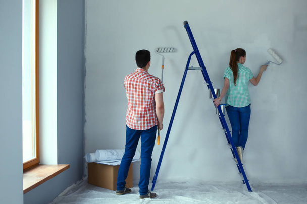 Portrait happy smiling young couple painting interior wall of new house. Young couple - 写真・画像