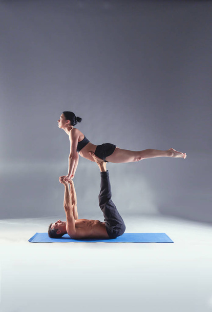 Young couple practicing acro yoga on mat in studio together. Acroyoga. Couple yoga. Partner yoga. - Fotó, kép