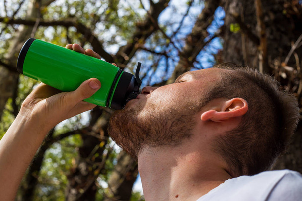 Een fitness-man, drankjes na het uitvoeren van in de natuur, zijn eiwitten uit  - Foto, afbeelding