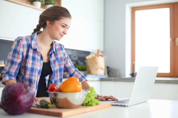 Young woman cutting vegetables in kitchen near desk. - Zdjęcie, obraz