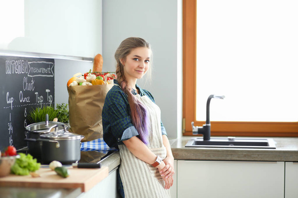 Young woman standing by the stove in the kitchen . - Фото, зображення
