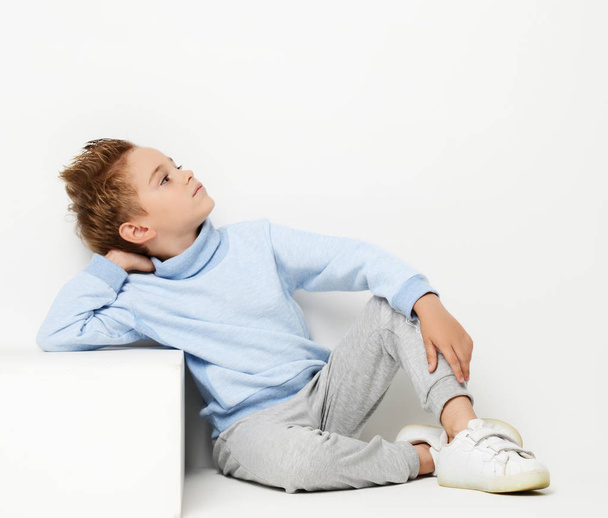 Happy young boy sitting in light blue sweater looking at the corner - Fotografie, Obrázek