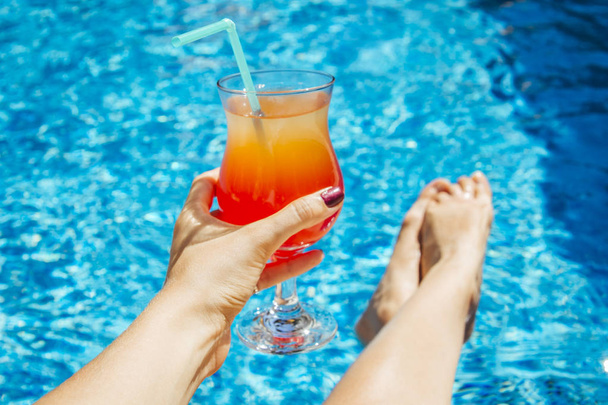 Жінка тримає коктейль на фоні басейну
 - Фото, зображення