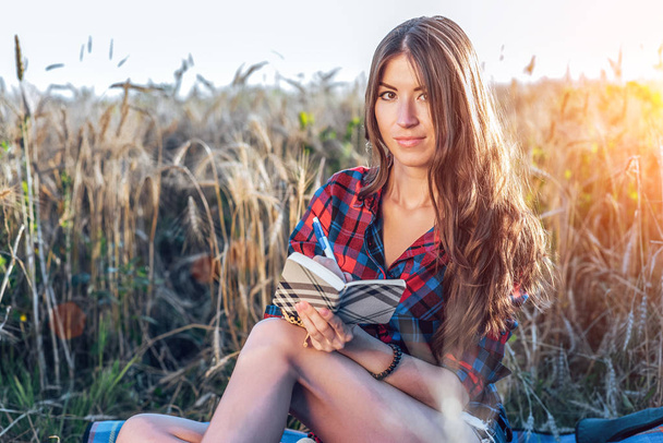 Beautiful brunette girl in field. Concept new ideas, outdoors, summer in nature. In his hand a notebook, long hair. Close-up. Portrait of a model. - Fotografie, Obrázek