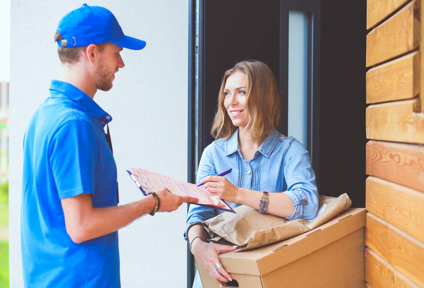 Smiling delivery man in blue uniform delivering parcel box to recipient - courier service concept. Smiling delivery man in blue uniform - Φωτογραφία, εικόνα