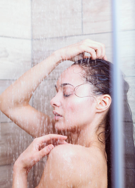 Young beautyful woman under shower in bathroom. - Foto, afbeelding