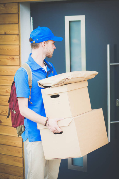 Repartidor sonriente con uniforme azul que entrega la caja de paquetes al destinatario: concepto de servicio de mensajería. Repartidor sonriente en uniforme azul - Foto, Imagen