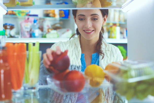 Portrait of female standing near open fridge full of healthy food, vegetables and fruits. Portrait of female - 写真・画像
