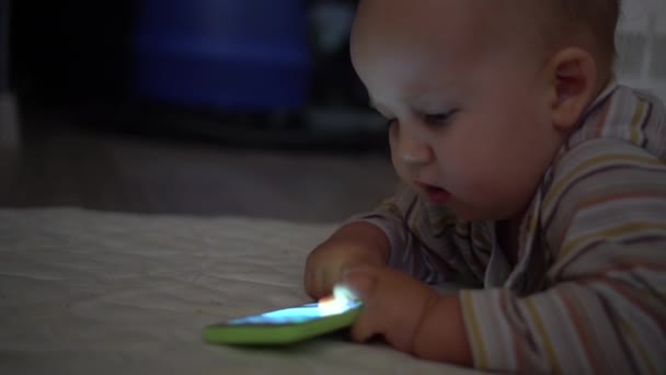 Baby plays with smartphone and pushes the button. Blue light on face. Handheld shot - 映像、動画