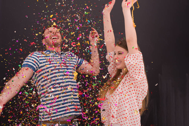 couple blowing confetti in the air isolated over gray - Foto, afbeelding