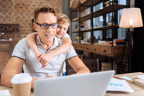 Affectionate boy hugging his father busy with work - 写真・画像