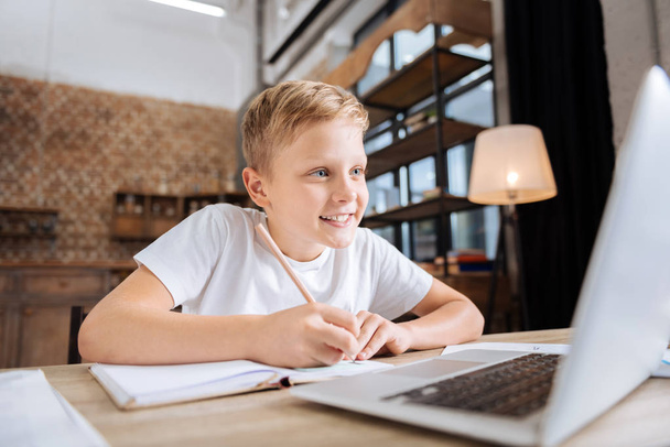 Cheerful boy copying information from laptop to notebook - Foto, Bild