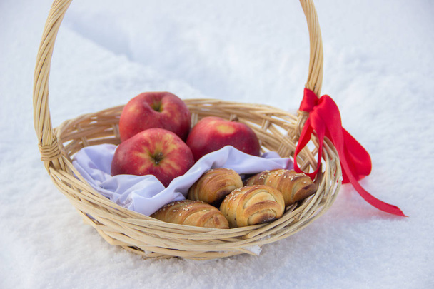 Koszyku słomy z wstążki z czerwoną czapkę z ciasta i jabłka na śniegu - Zdjęcie, obraz