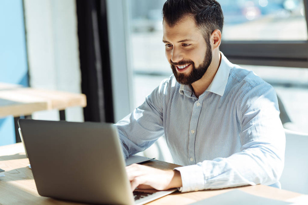 Pleasant smiling man using his laptop in office - Photo, image